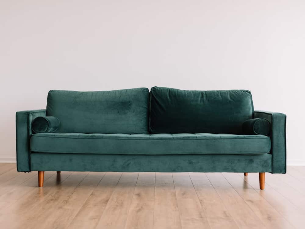 Sofá de terciopelo verde sobre suelo de madera en una sala diáfana
